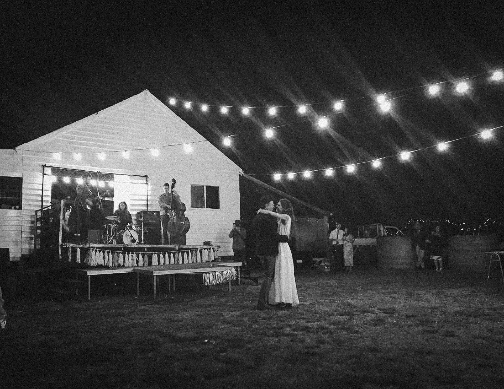 Couple sharing their first dance at an outdoor wedding reception with live band and string lights